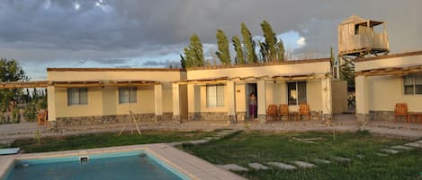 A poolside view of a building with a pool, outdoor seating, and a wooden structure on stilts.