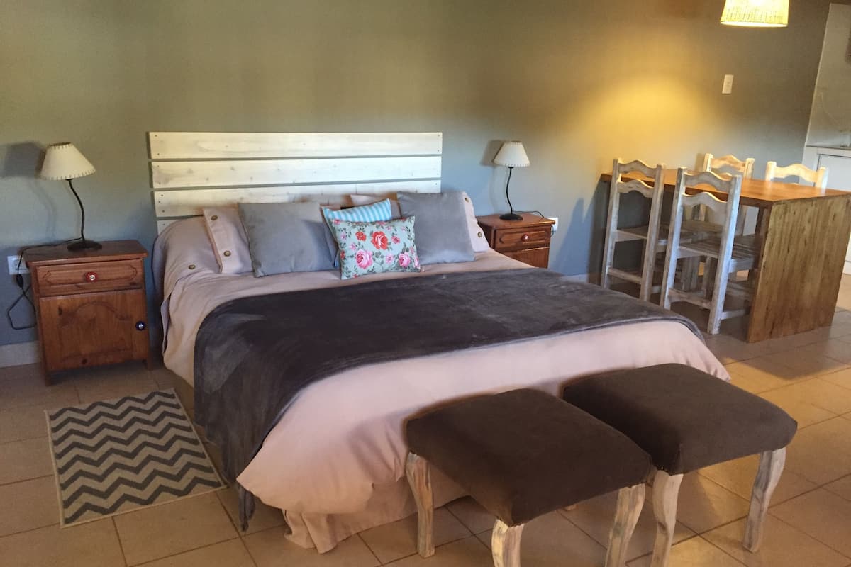 Un dormitorio con una cama, dos mesitas de noche, un aparador, un tocador y un banco.