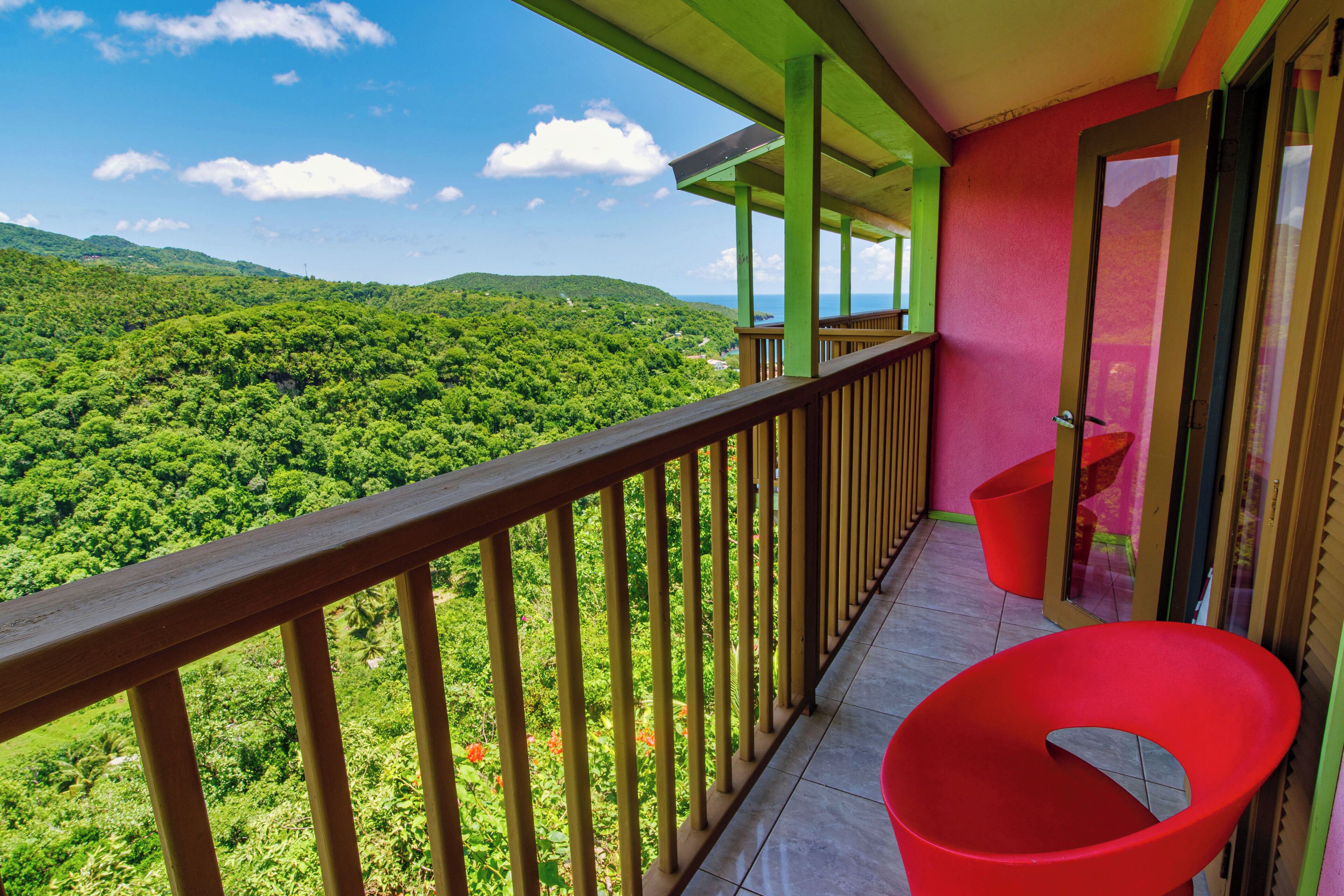 Un balcón con vistas a un paisaje verde exuberante, una silla roja y una puerta con panel de vidrio.