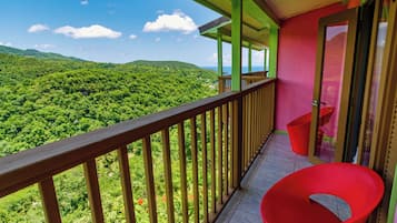 Un balcón con vistas a un paisaje verde exuberante, una silla roja y una puerta con panel de vidrio.