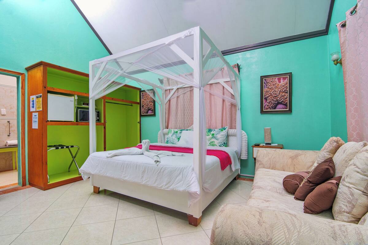 A bedroom with a four-poster bed, a sofa, and a green wall.