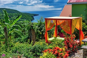 Um jardim com uma canteira de flores vermelhas, um banco de madeira e um toldo.