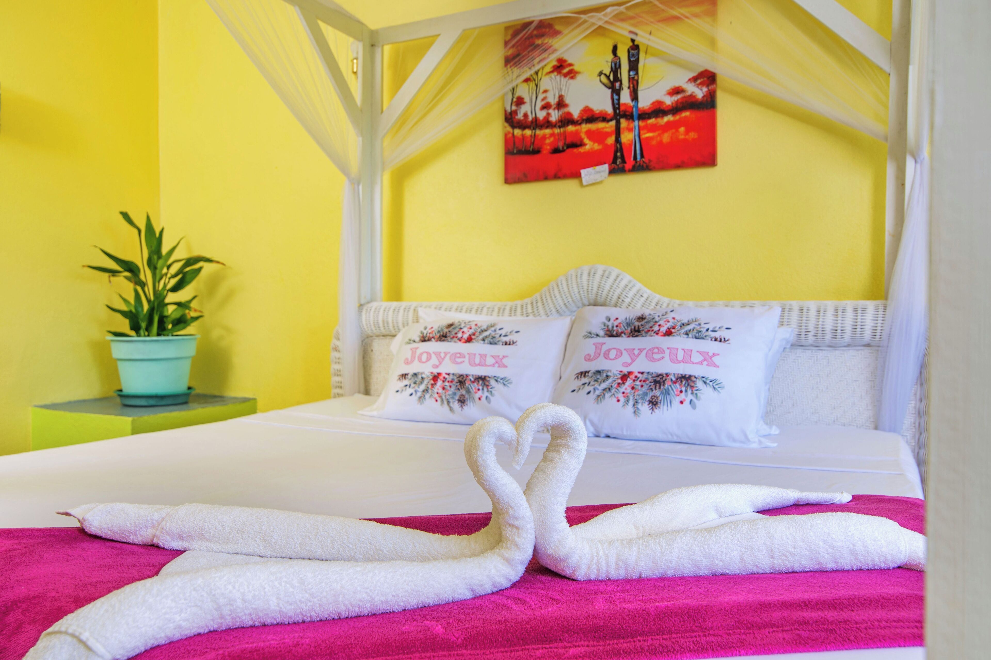 Una cama con ropa blanca, dos almohadas con motivos florales y una toalla rosa.