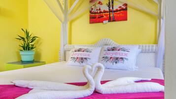 Una cama con ropa blanca, dos almohadas con motivos florales y una toalla rosa.