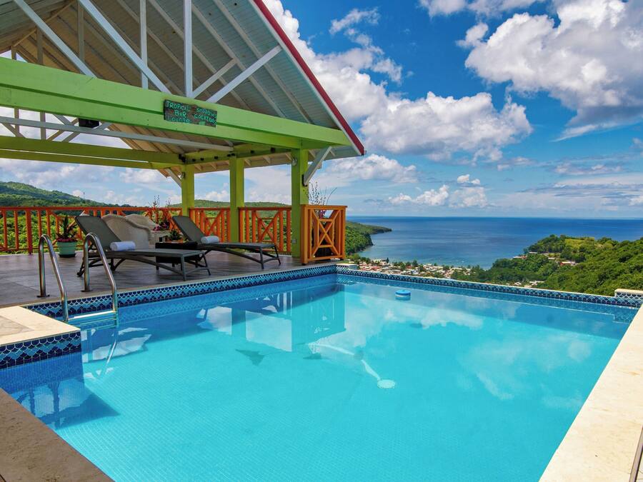 A swimming pool with a covered area, a view of the sea, and a tropical landscape.