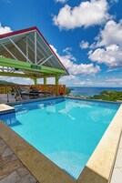 Uma piscina com área coberta, vista para o mar e paisagem tropical.