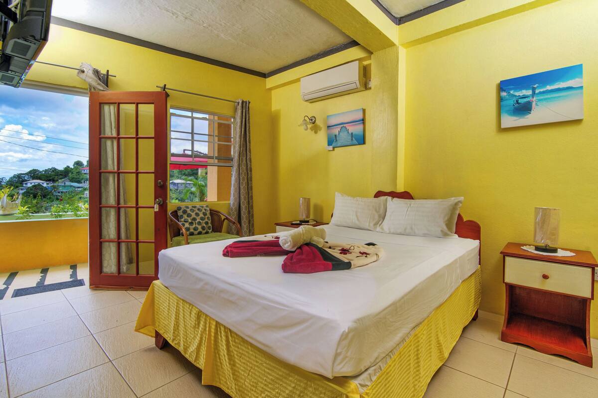 A hotel room with a bed, a nightstand, a chair, and a window with a view of the outside.
