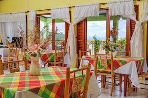 Um restaurante com mesas cobertas por toalhas quadriculadas coloridas, cadeiras de madeira e cortinas brancas.