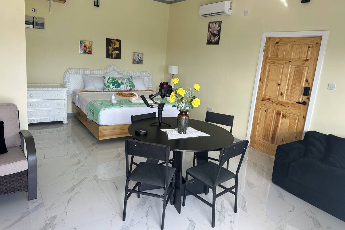 A hotel room with a bed, a dining table with chairs, a sofa, and a wooden door.