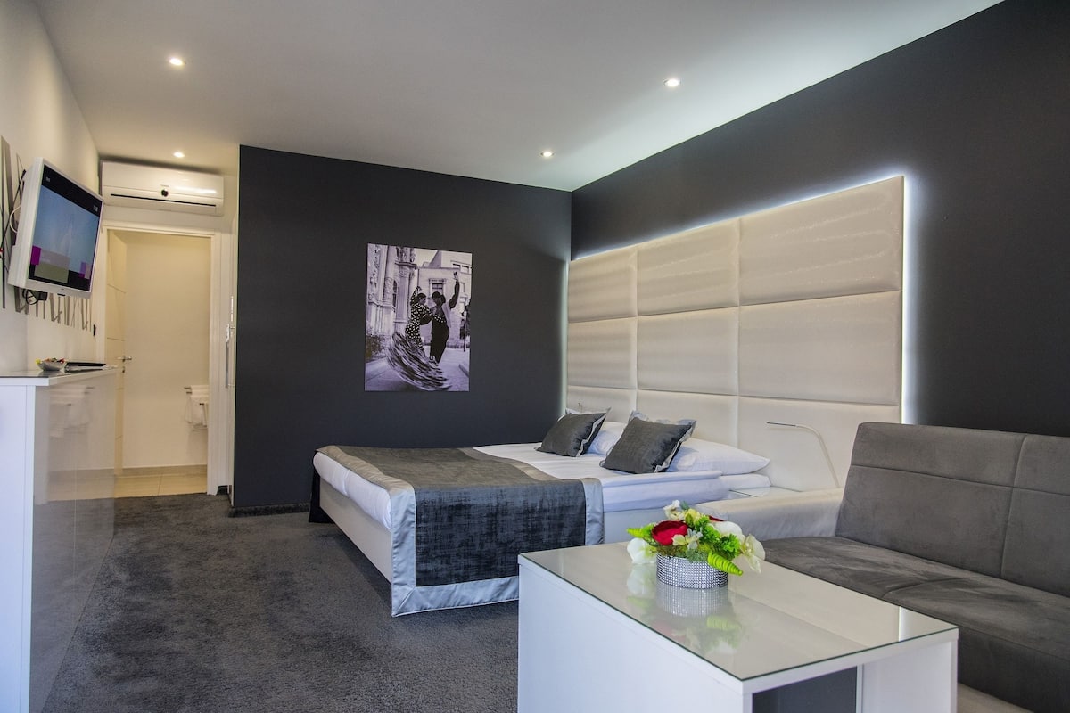 A modern hotel room with a bed, a sofa, a coffee table, and a TV.