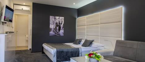 Una habitación de hotel moderna con cama, sofá, mesa de centro y televisión.
