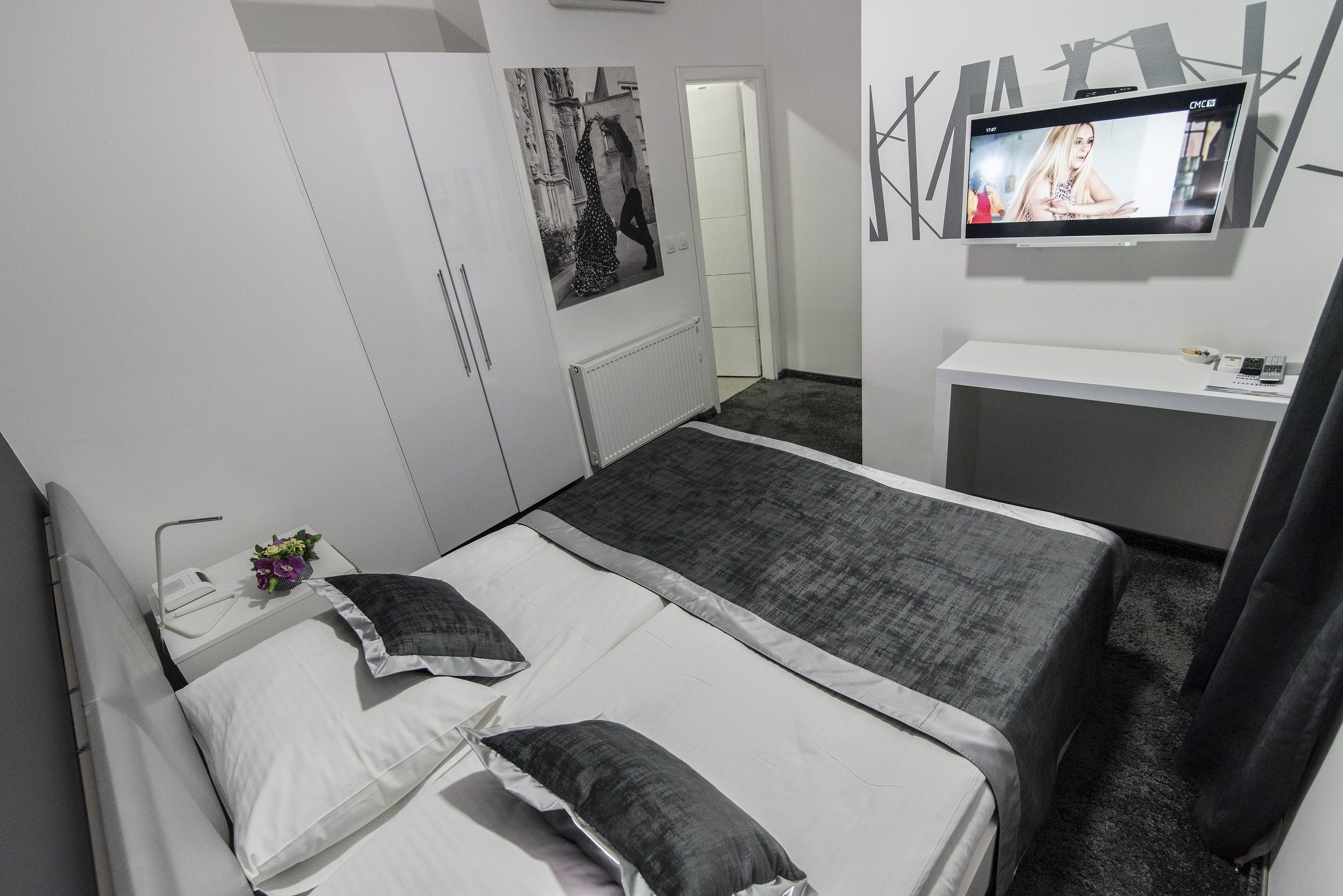 A bedroom with a bed, a TV, a wardrobe, and a small table with a flower.
