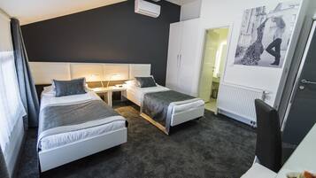 A modern hotel room with two single beds, a desk, a chair, a radiator, and a wall-mounted air conditioner.
