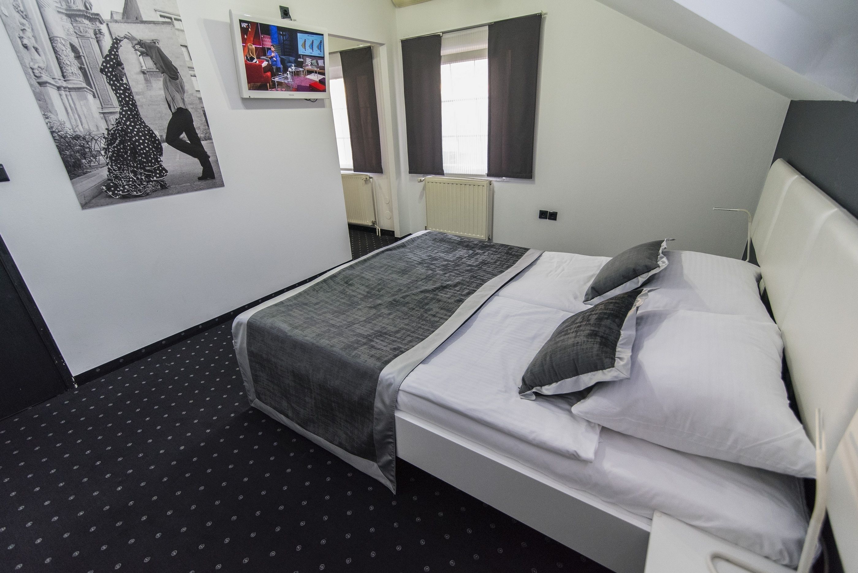 Une chambre d’hôtel avec un lit, une fenêtre avec des rideaux, un radiateur et un téléviseur fixé au mur.