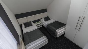 Une petite chambre d’hôtel moderne, dotée de deux lits simples, d’une armoire blanche et d’un sol noir à motifs.