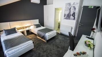 Una habitación de hotel moderna con dos camas individuales, un escritorio con computadora, una silla y una pequeña mesa con flores.