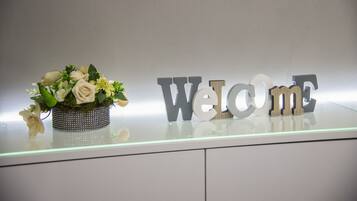 Un área de recepción con un letrero de 'Welcome' y un arreglo floral decorativo sobre una barra de vidrio.