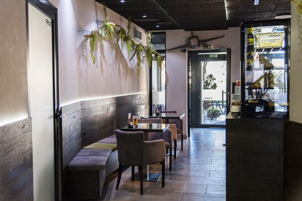 Interior de un restaurante con disposición de mesas, un reloj en la pared y un refrigerador con botellas.