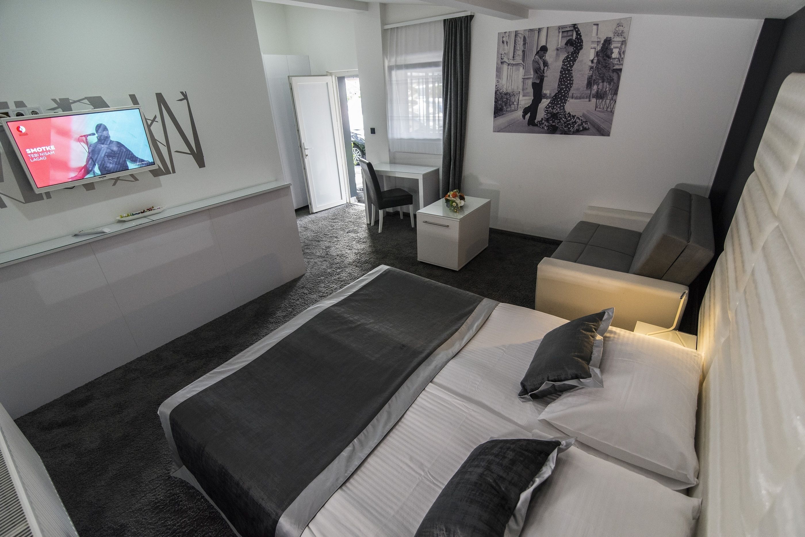 A modern hotel room with a large bed, a desk, a chair, and a TV mounted on the wall.