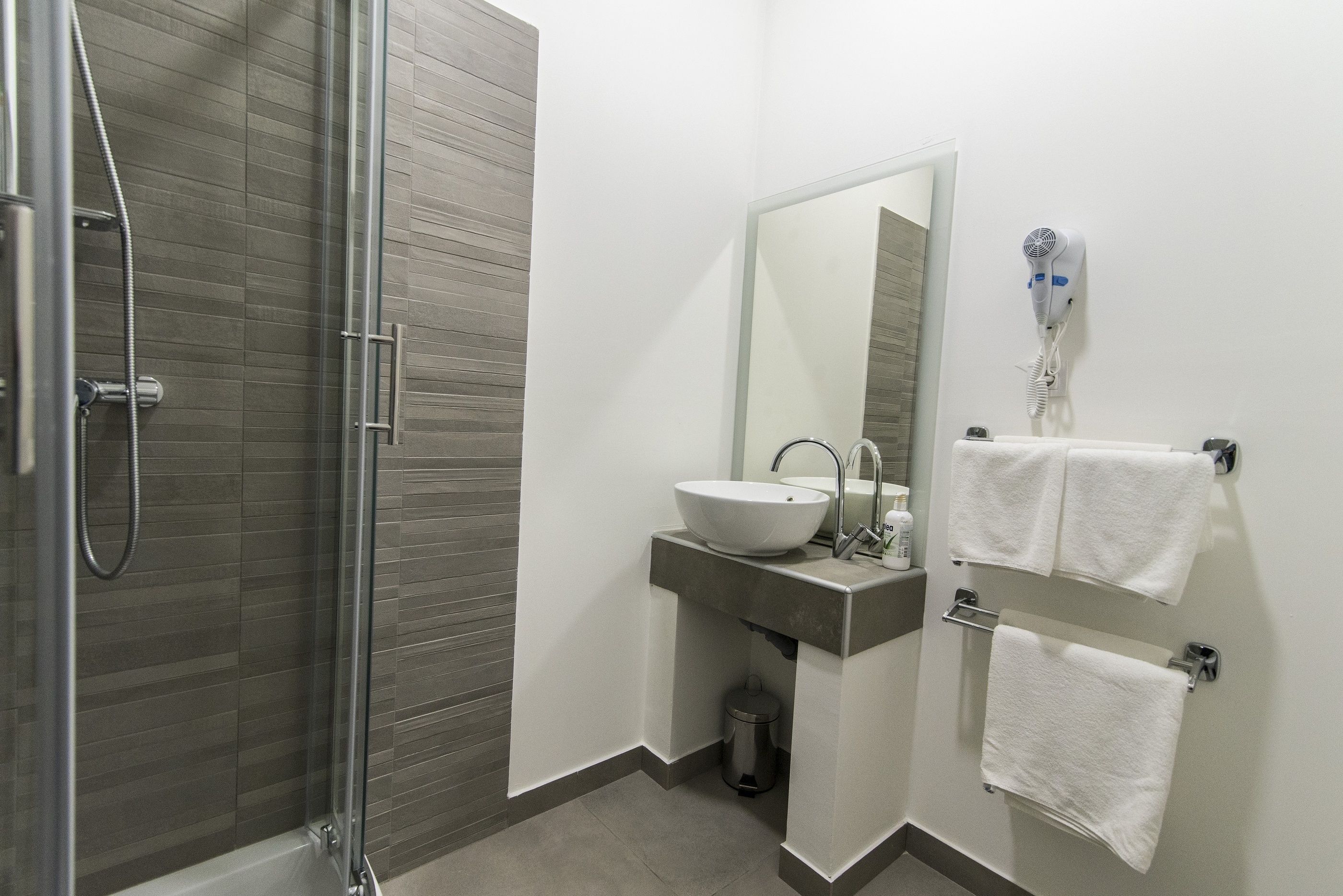 A modern bathroom with a glass shower enclosure, a sink with a mirror, and a hairdryer mounted on the wall.