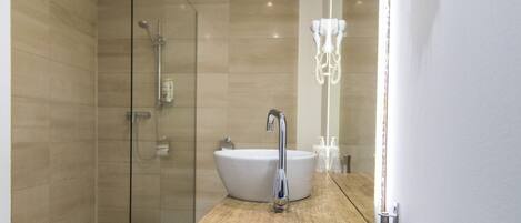 Un baño moderno con ducha envuelta en vidrio, un lavabo blanco y una encimera de madera.