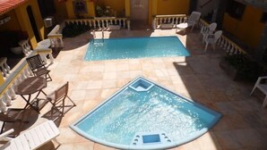 A swimming pool area with two pools, surrounded by lounge chairs and tables. - Pousada Pratagy (Saquarema)