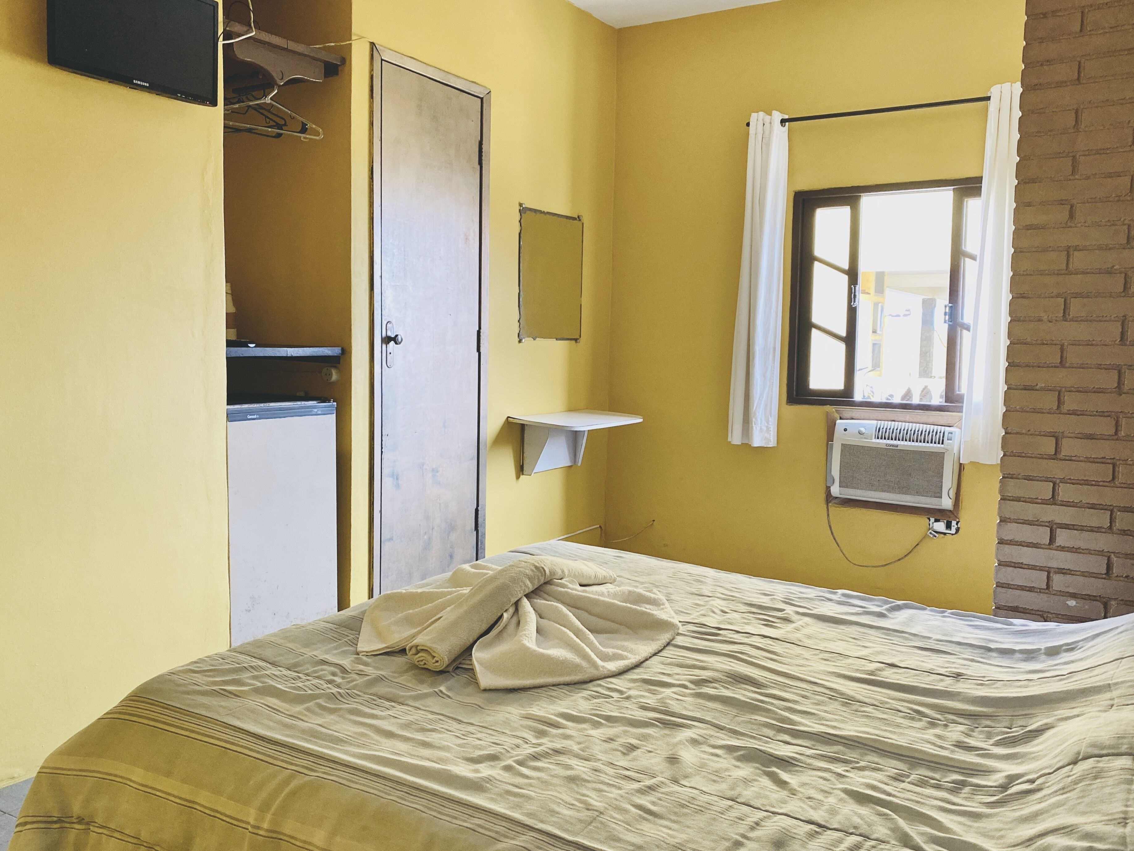 A room with a bed, a wardrobe, a mirror, a window with a curtain, and a radiator.