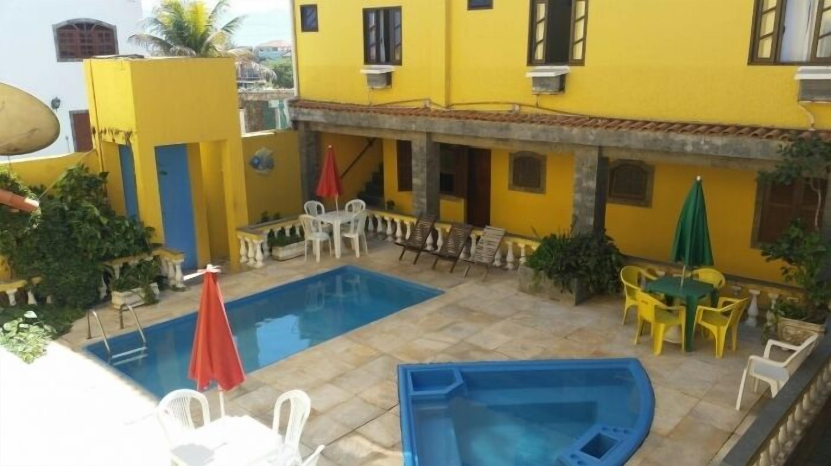 Un patio con piscina, mobiliario exterior y edificios de color amarillo.