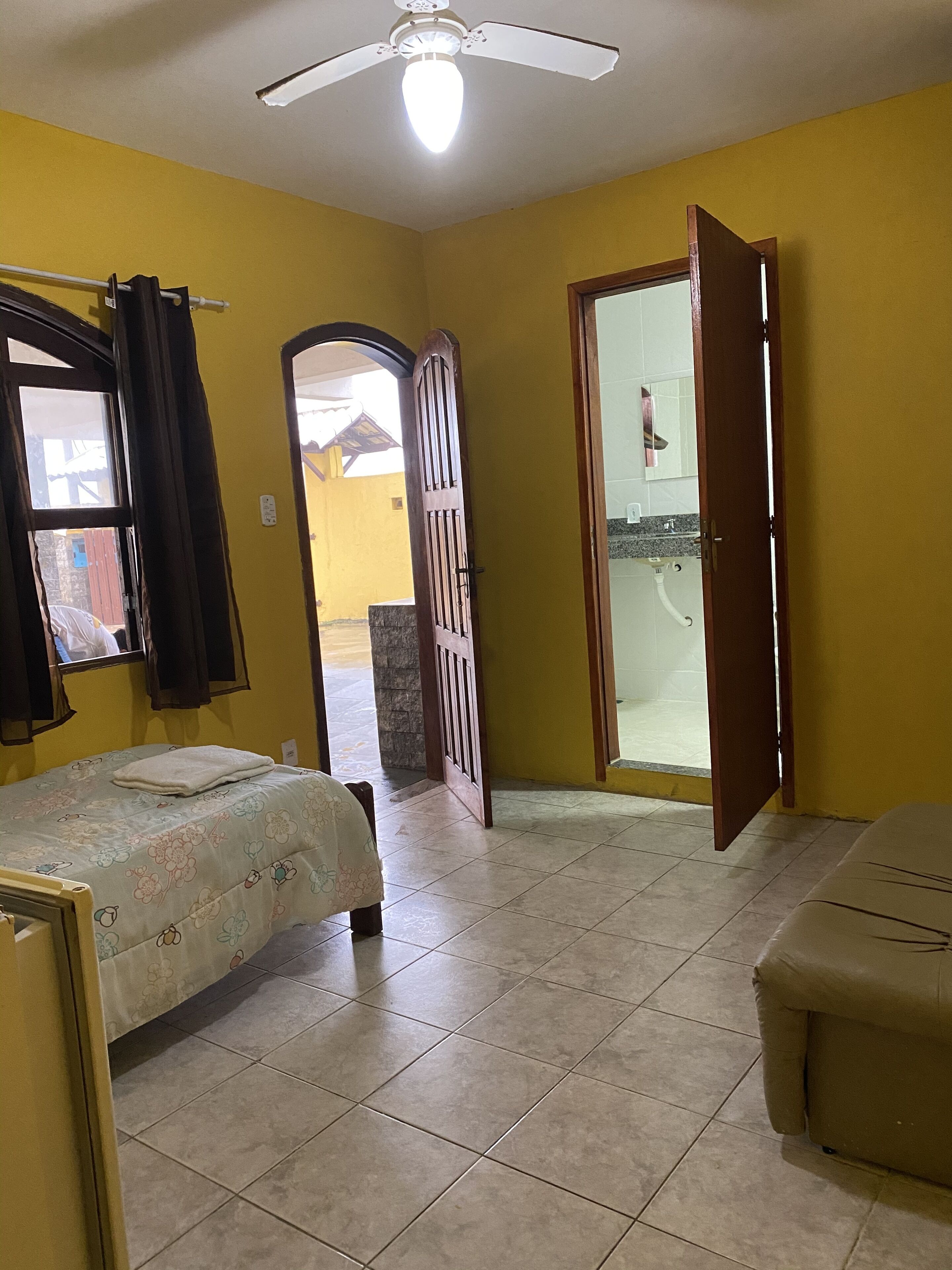 Une pièce comprenant un lit, un canapé, un ventilateur de plafond et une salle de bain visible à travers une porte ouverte.