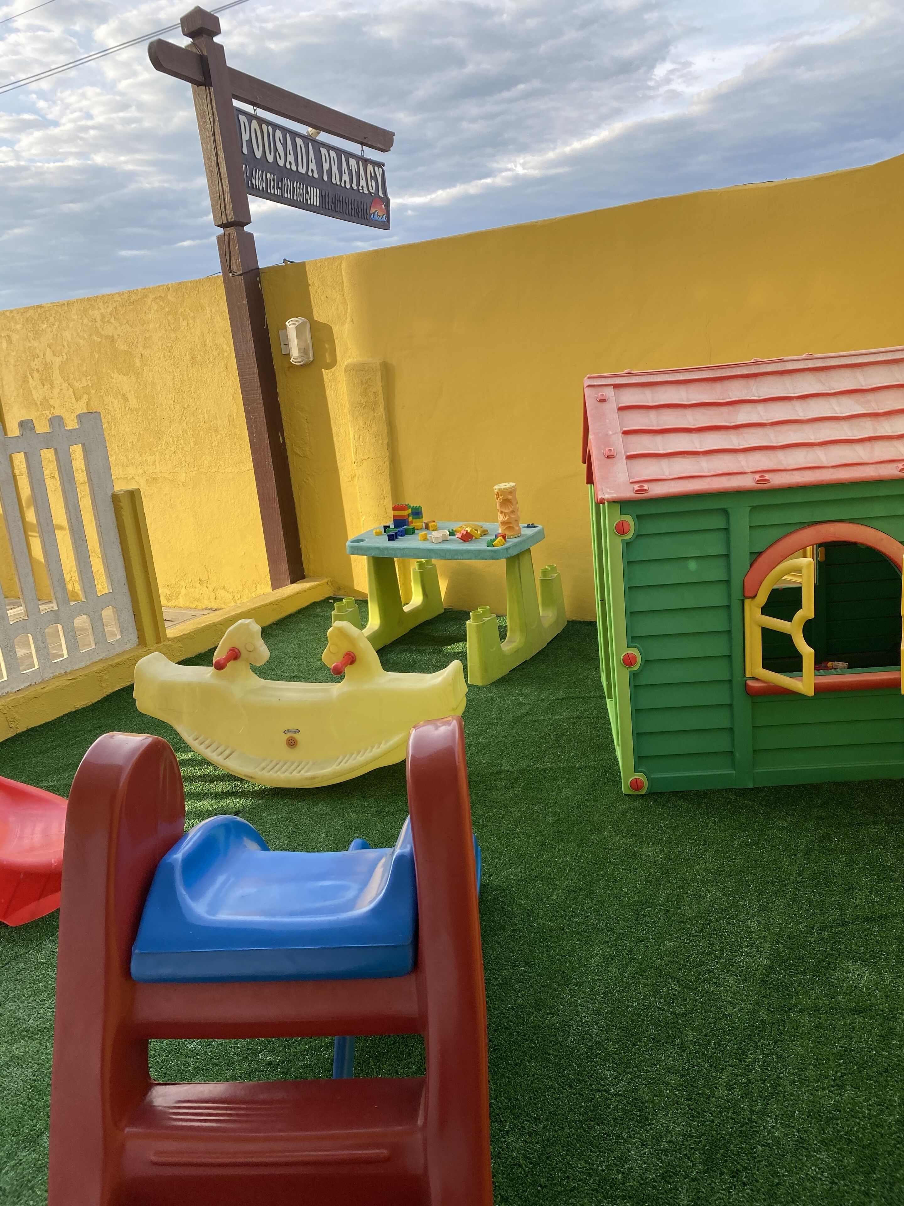 Zona infantil con un tobogán, una mesita con juguetes y una casita de juegos.