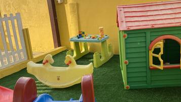 Zona infantil con un tobogán, una mesita con juguetes y una casita de juegos.