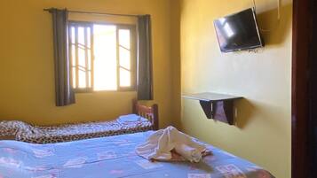 Una camera da letto con due letti, una televisione fissata al muro e una finestra con tende.