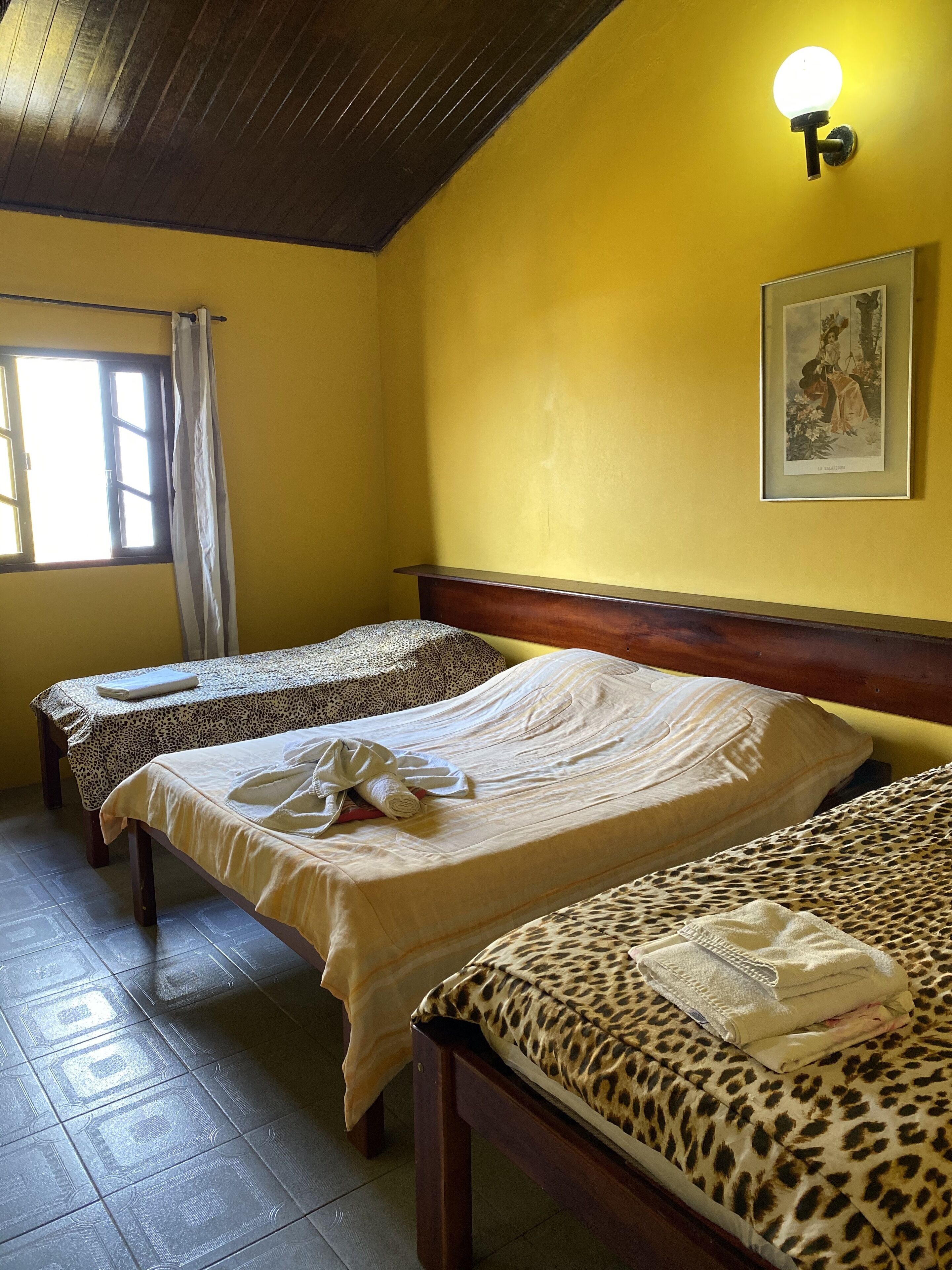 Habitación de hotel con dos camas, cabecera de madera, un cuadro enmarcado en la pared y una ventana con cortinas.