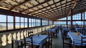A spacious dining area with tables and chairs, large windows, and a high ceiling. - Pousada Pratagy (Saquarema)