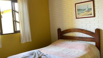Un lit simple avec une tête de lit en bois, dans une pièce aux murs jaunes et à un mur en briques blanches.