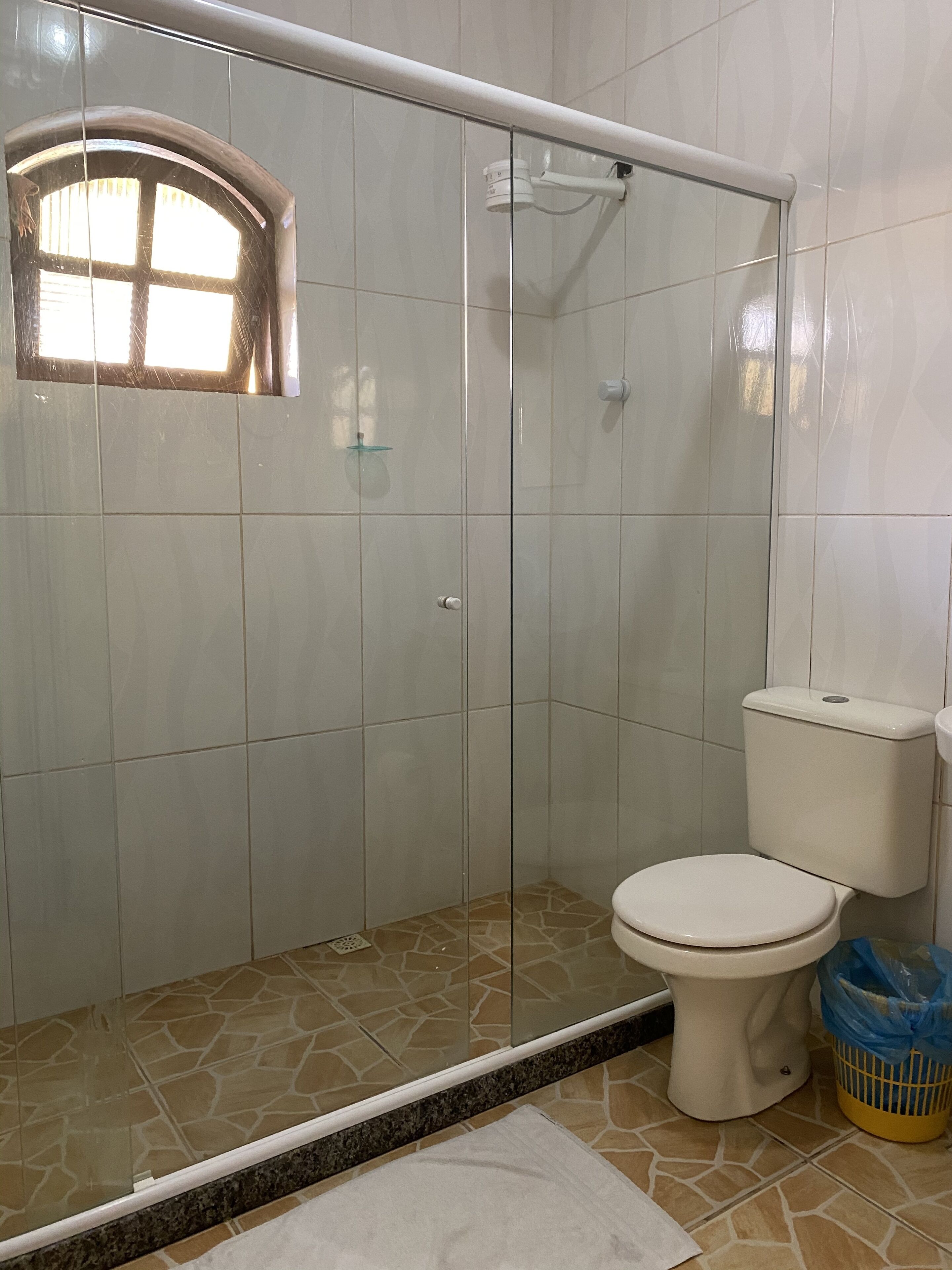 A bathroom with a glass-enclosed shower, a toilet, and a small window.
