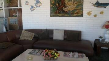 A living room with a brown leather sofa, a coffee table with magazines and a floral arrangement, and a wall with decorative fish and a painting.