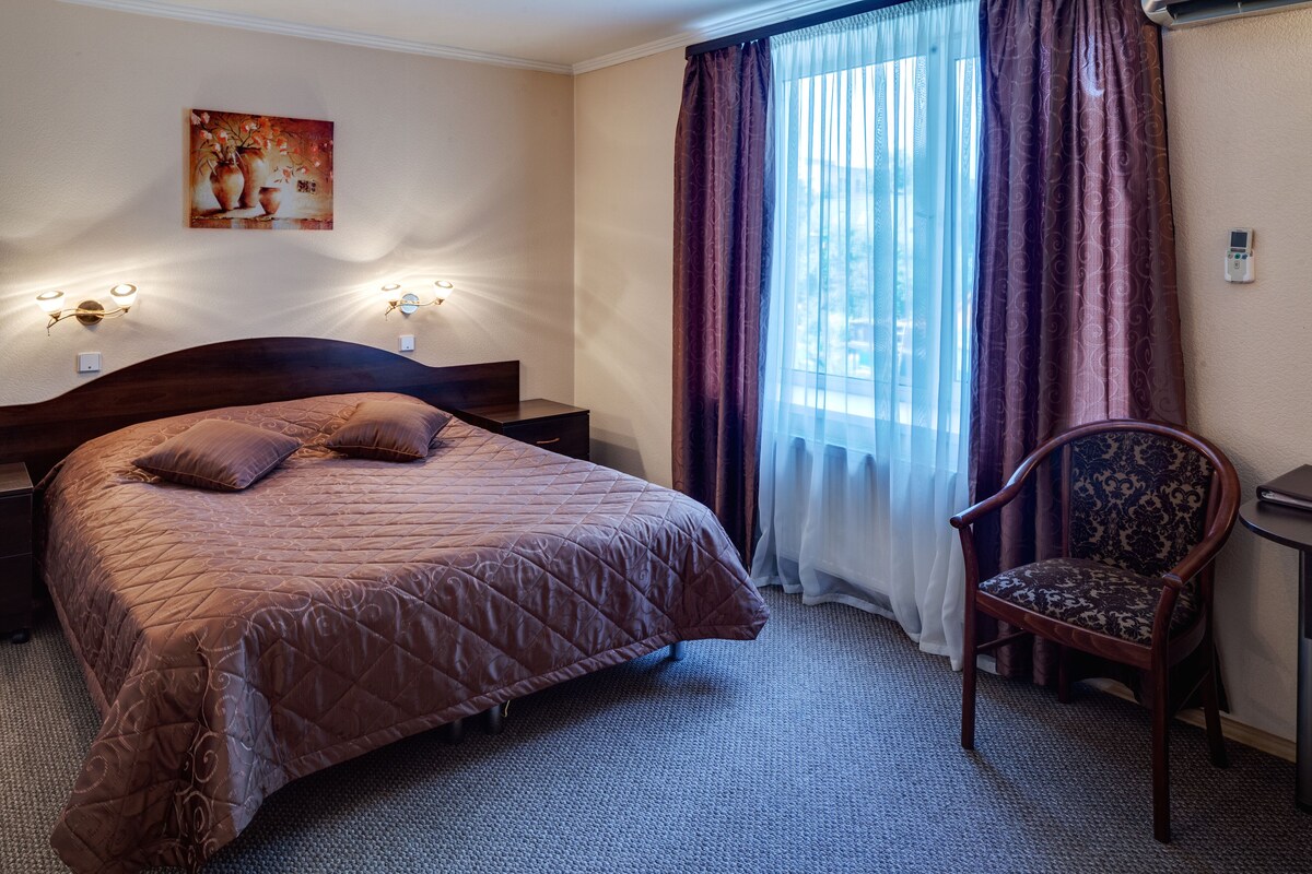 A hotel room with a large bed, a chair, a desk, and a painting on the wall.
