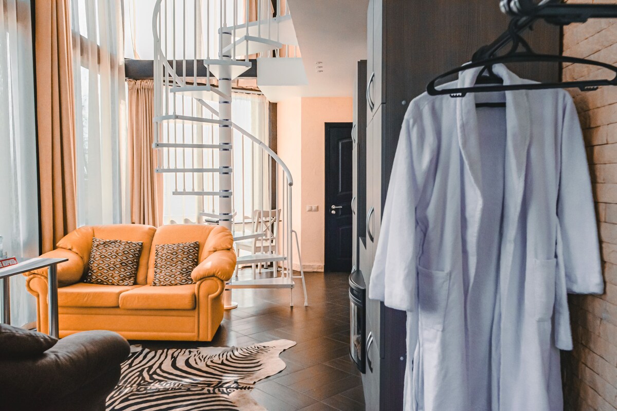 A modern hotel room with a spiral staircase, a sofa, a zebra-patterned rug, and a white robe hanging on the wall.