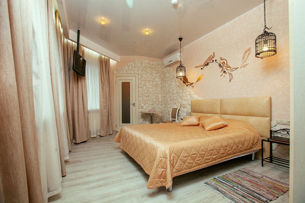 A bedroom with a large bed, a stone accent wall, a television, and a hanging light fixture.
