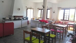 Un vaste espace de salle à manger avec plusieurs tables et chaises, un coin cuisine équipé d’appareils électroménagers et de grandes fenêtres laissant entrer la lumière naturelle.