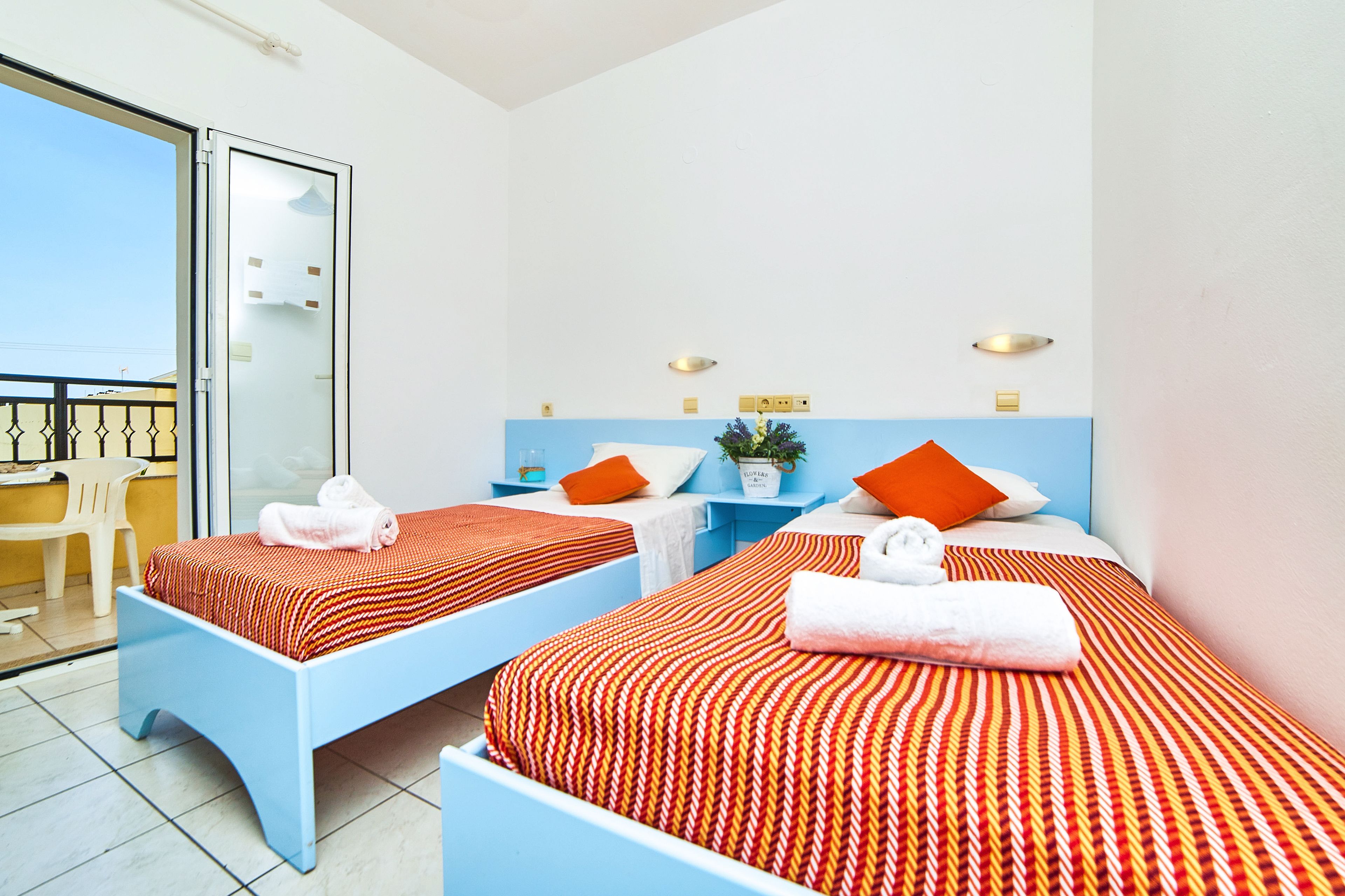 A hotel room with two beds, each with a red and white striped bedspread, a small table with a plant, and a chair.