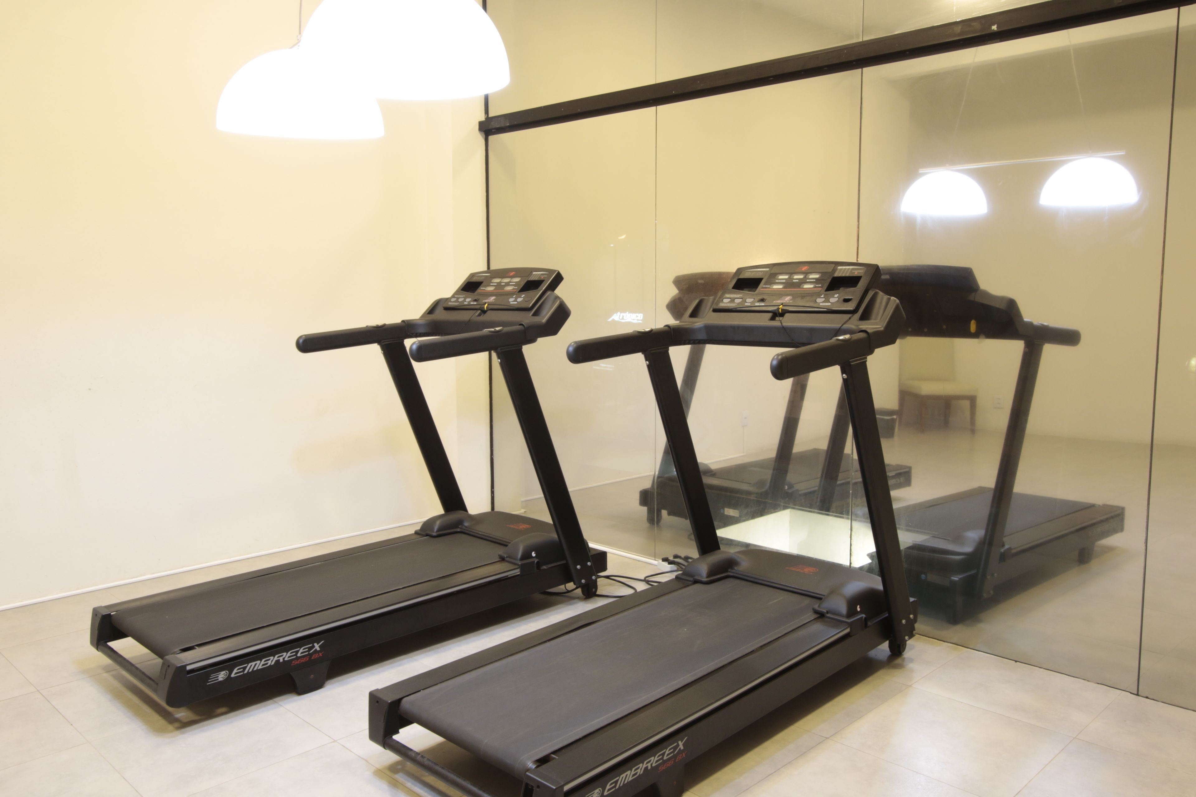 Tres cintas de correr en una sala con pared de vidrio y una lámpara en el techo.