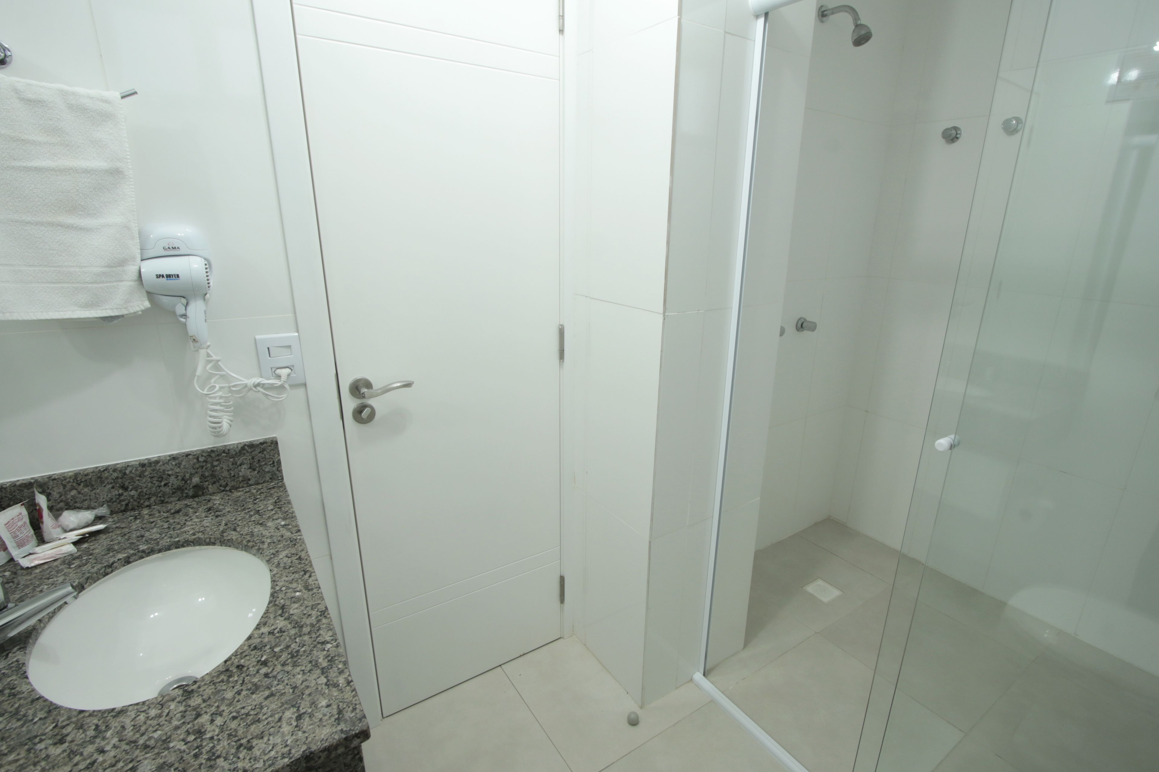 A bathroom with a granite countertop, a white sink, a hairdryer, and a glass-enclosed shower.