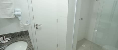 A bathroom with a granite countertop, a white sink, a hairdryer, and a glass-enclosed shower.