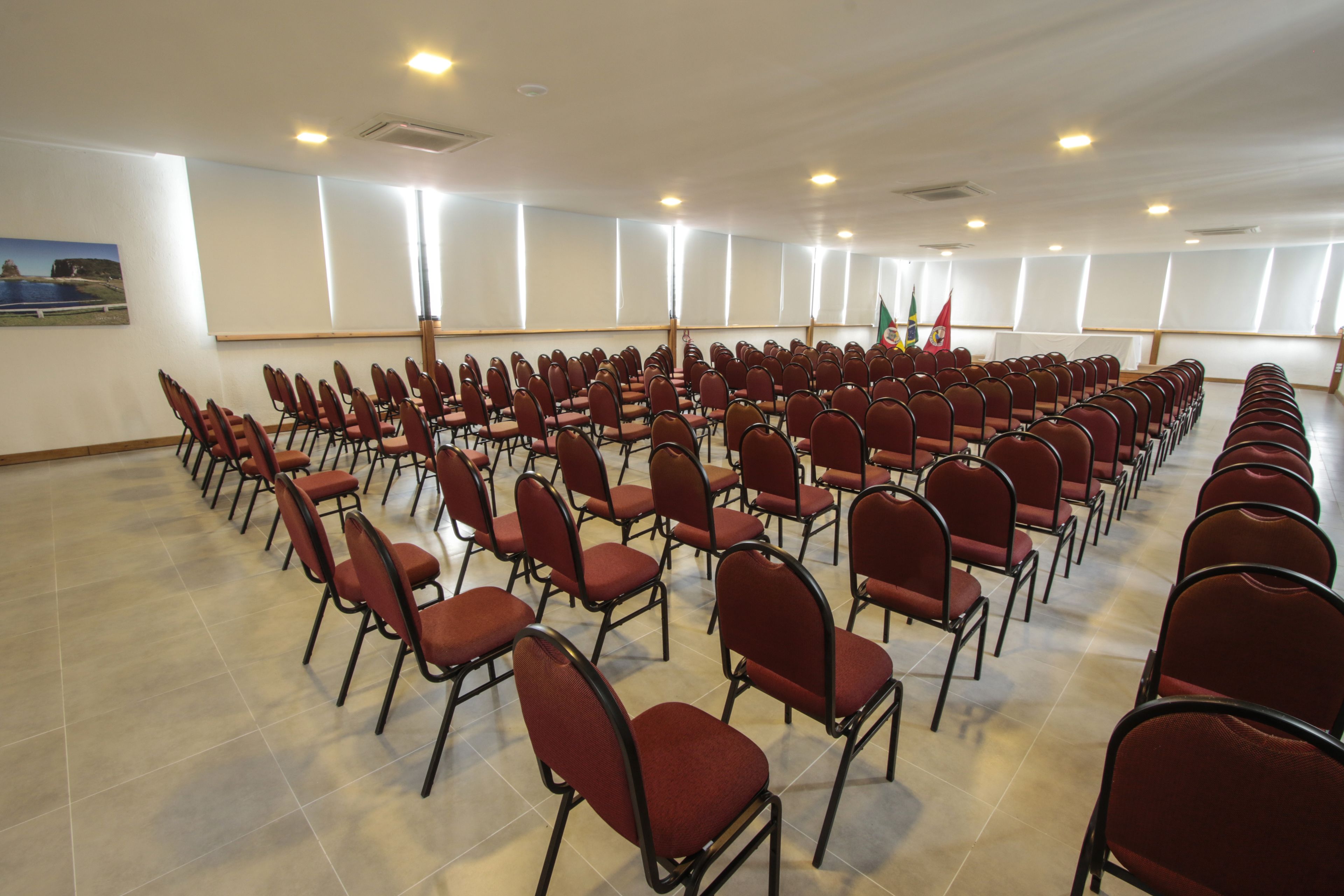 A conference room with rows of red chairs, large windows, and a flag on the wall.