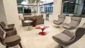 A modern lounge area with multiple seating options, including sofas and chairs, a red table, and a potted plant.
