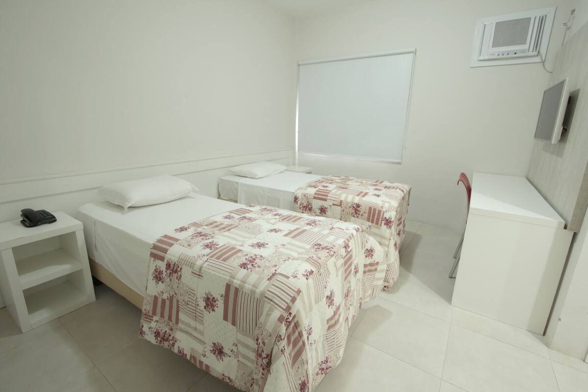 Une chambre d’hôtel avec deux lits, un bureau, une chaise, une petite table et une armoire.