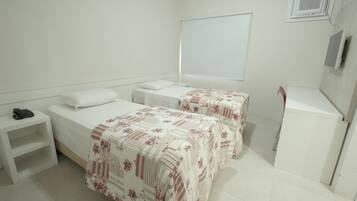 Habitación de hotel con dos camas, un escritorio, una silla, una mesita pequeña y un armario.