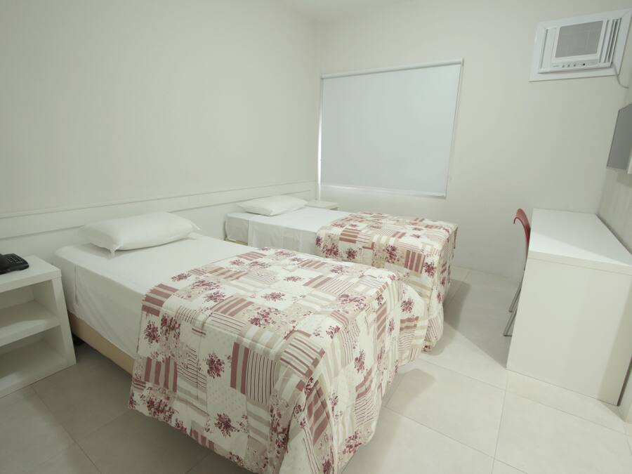 Habitación de hotel con dos camas, un escritorio, una silla, una mesita pequeña y un armario.